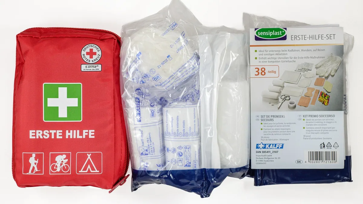 A compact red first aid kit for travel laid open beside its plasters and dressings