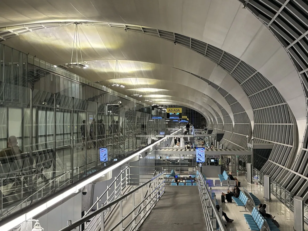 The long curved glass-and-steel concourse of Suvarnabhumi Airport at night, with gates and seating below