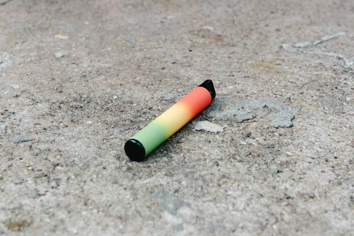 A brightly coloured disposable vape lying on a concrete surface