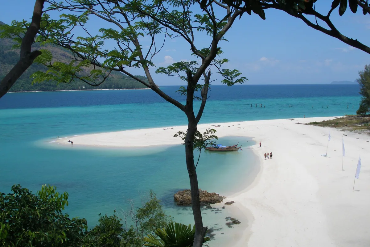White sand spit curving into turquoise water on Koh Lipe, with a longtail boat moored in the shallows