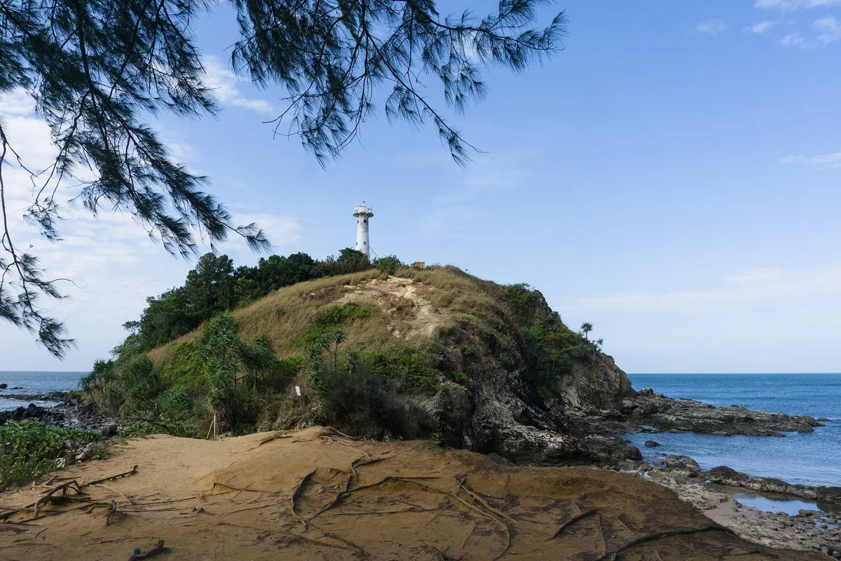 White lighthouse on a grassy headland above the sea at the southern tip of Mu Ko Lanta National Park