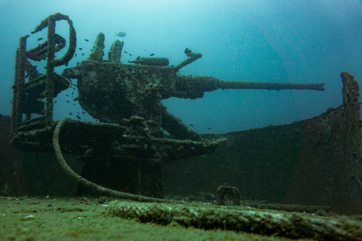 Deck gun on the sunken HTMS Sattakut wreck in blue-green water, a popular dive site off Koh Tao
