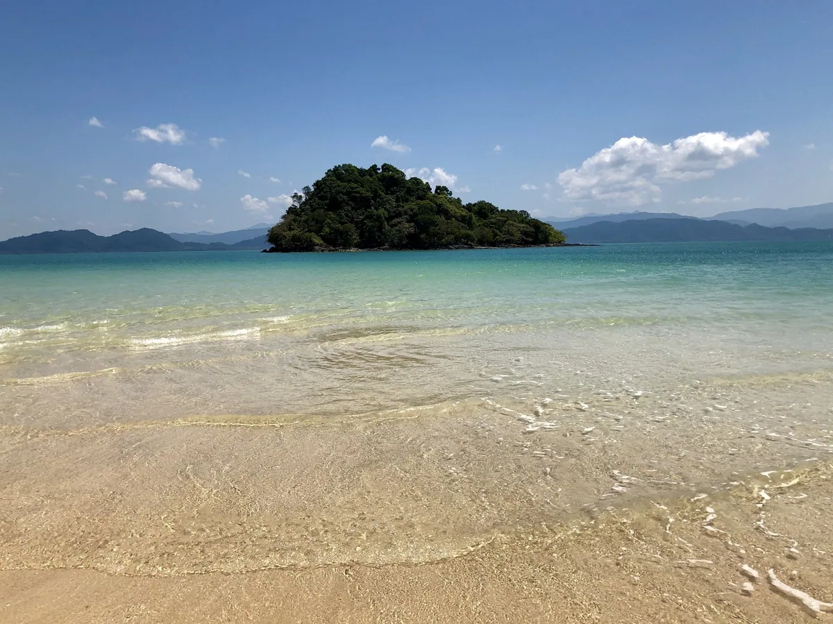Clear turquoise shallows off a Koh Phayam beach facing a small wooded islet and distant hills