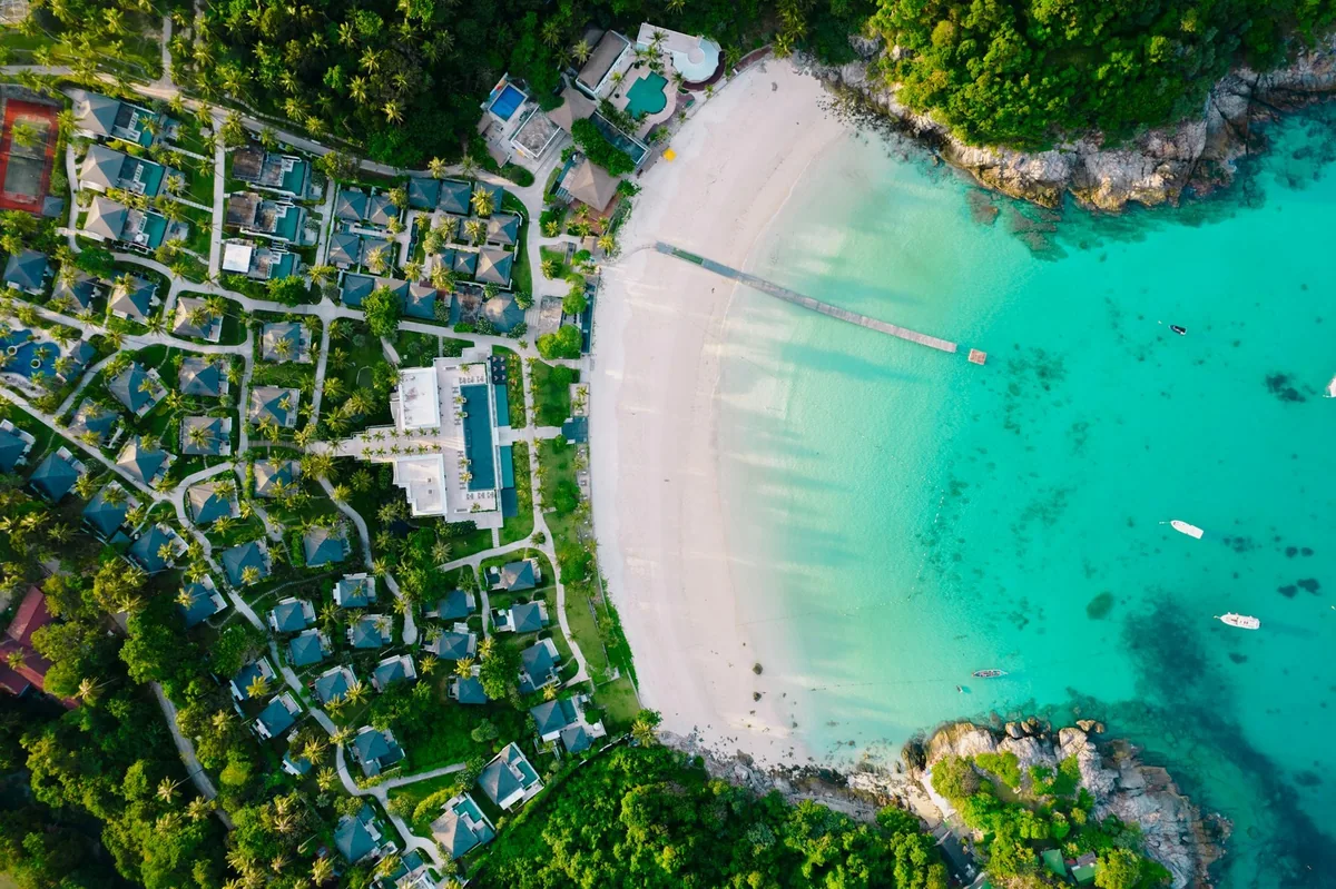 Aerial view of the white sand and turquoise water of Patok Bay on Koh Racha Yai, with its long pier and beachfront villas