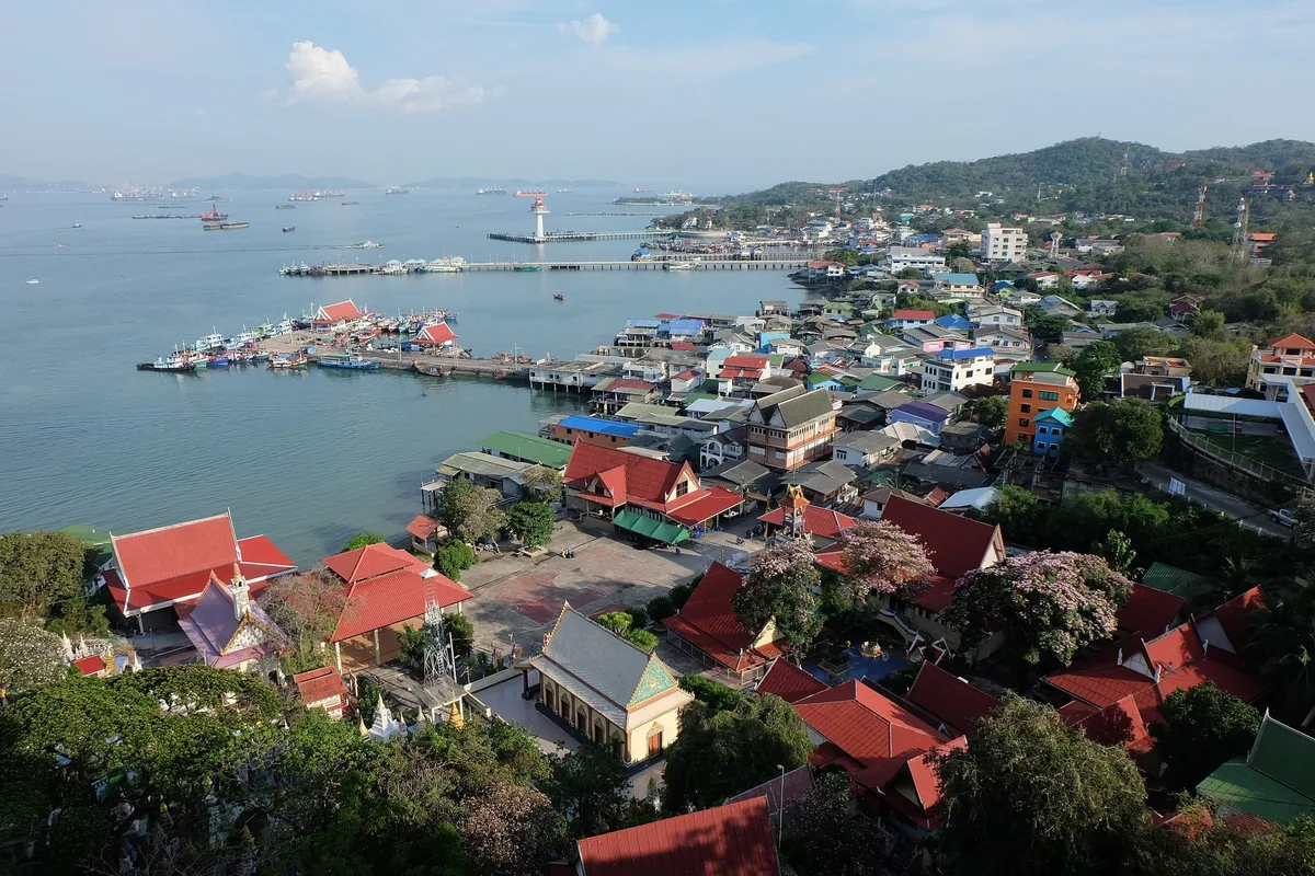 Red temple roofs and the harbour town of Ko Si Chang with piers, fishing boats and anchored cargo ships beyond