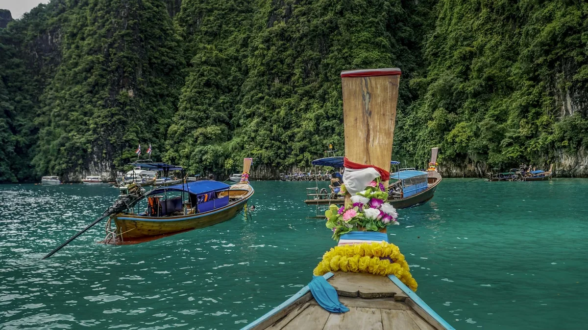 Garlanded longtail boat bow in the emerald water of Pileh Lagoon beneath jungle cliffs