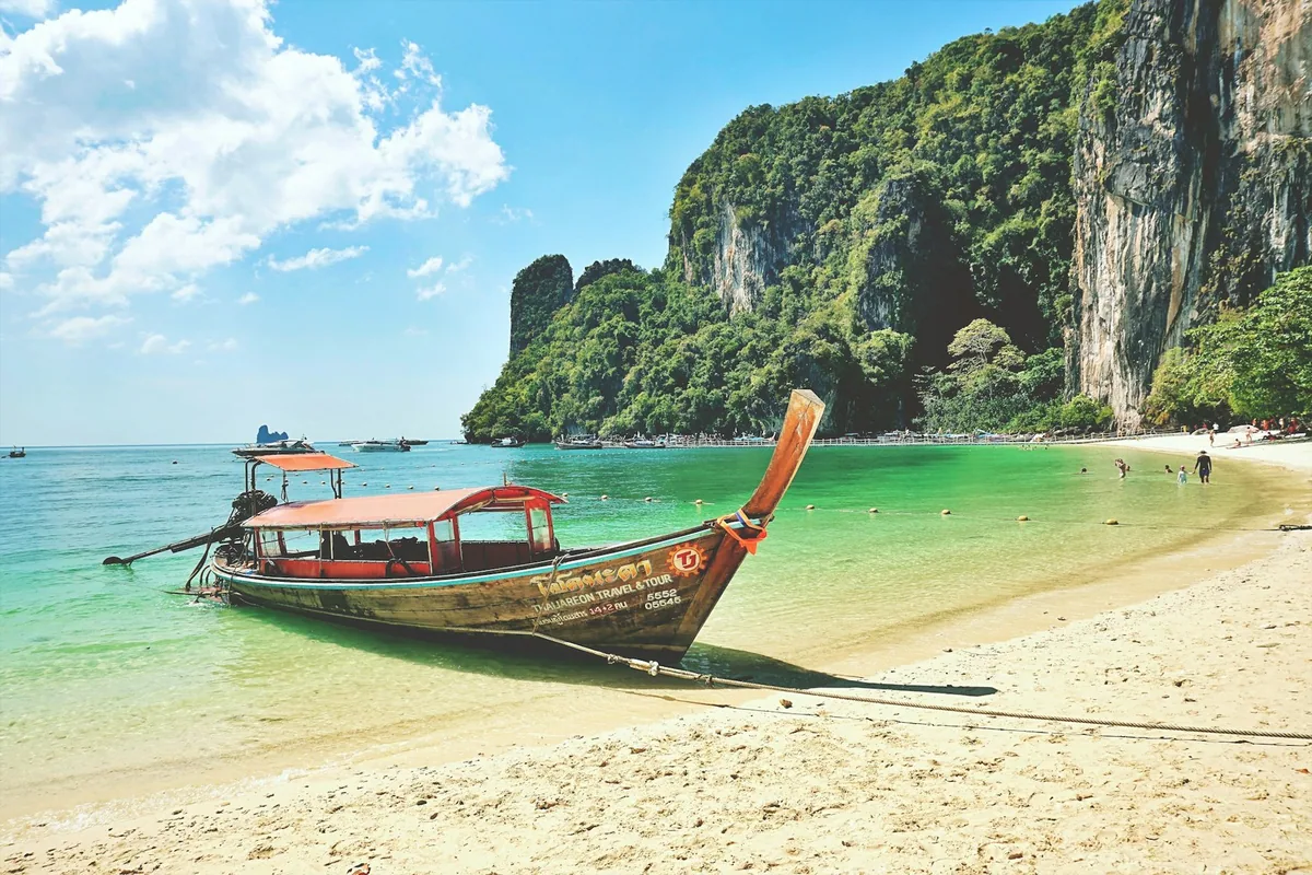 Longtail boat pulled up on a sandy beach below limestone cliffs on Ko Hong, Krabi