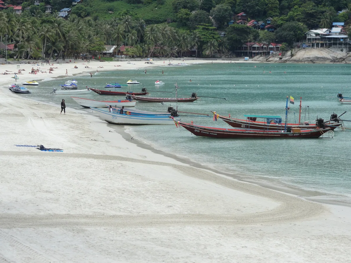 Longtail boats pulled up on the white sand of Haad Rin Sunrise Beach, the Full Moon Party beach on Koh Phangan