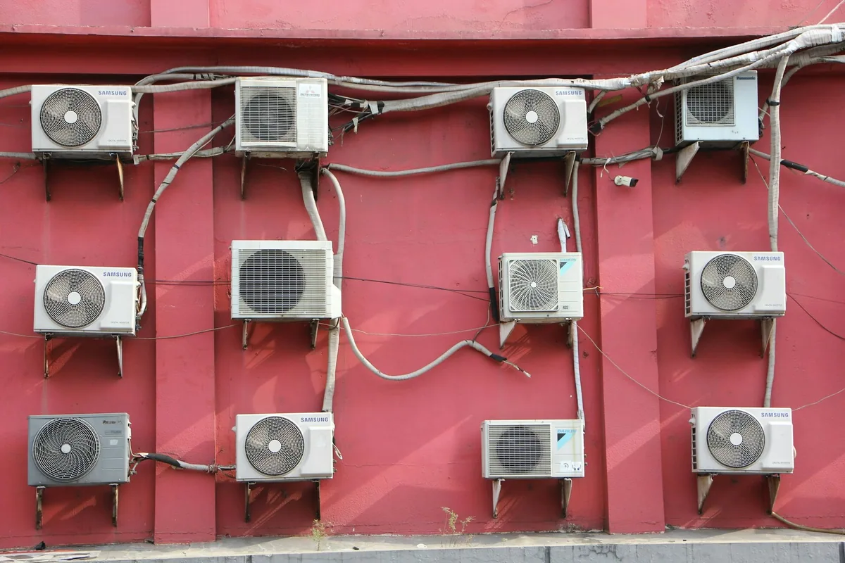 Rows of outdoor air conditioner units and their pipes fixed to a red-painted building wall