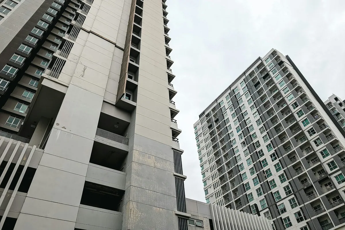 Looking up at two high-rise condominium towers with rows of balconies in Bangkok