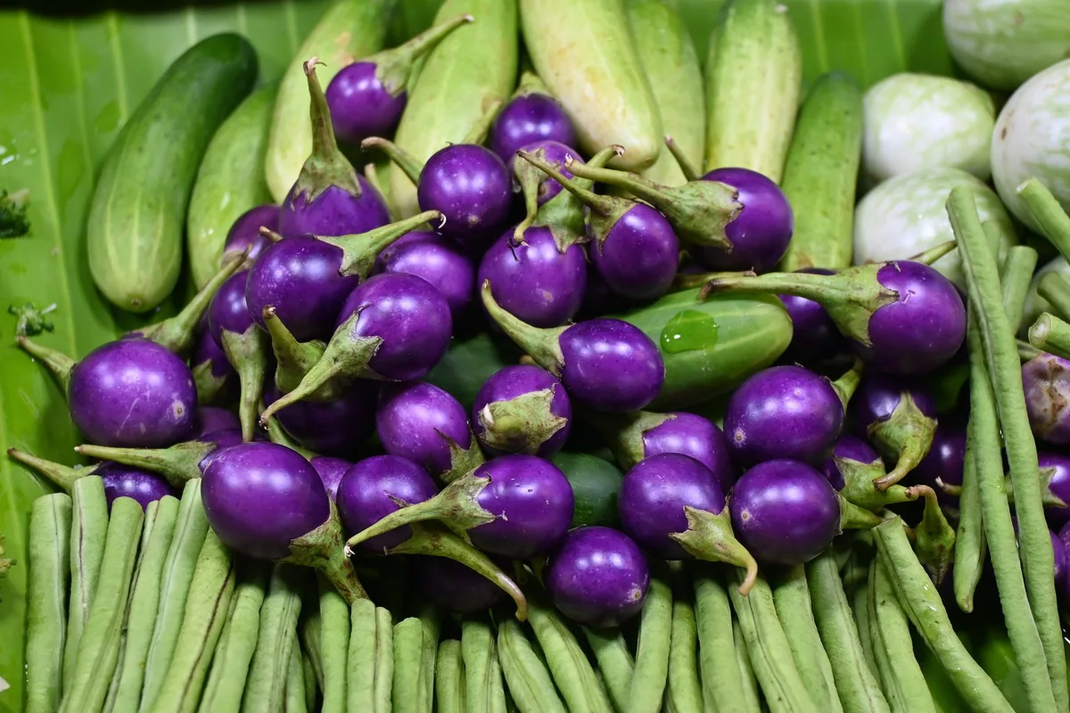 Round purple Thai eggplants piled with green beans and cucumbers at a market stall in Rayong