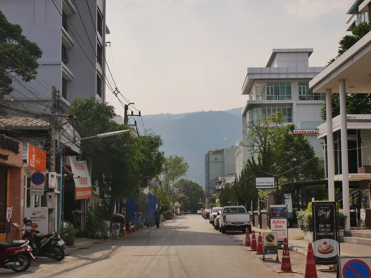 Street on Nimmanhaemin Road in Chiang Mai with hazy mountains rising beyond the buildings