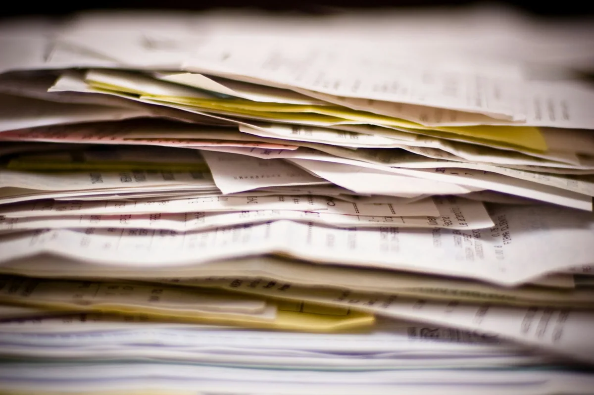 A thick stack of paper forms, receipts and statements piled up on a desk, waiting to be sorted