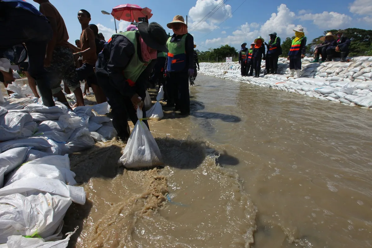 Volunteers laying white sandbags along a flooded road in Bangkok's Sai Mai district to hold back floodwater