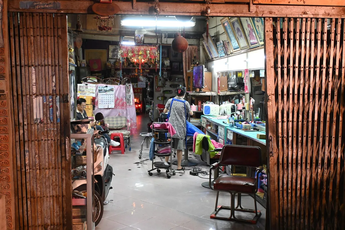 Barber at work late in the evening in a small Thai neighbourhood shop, framed behind its folding metal gate