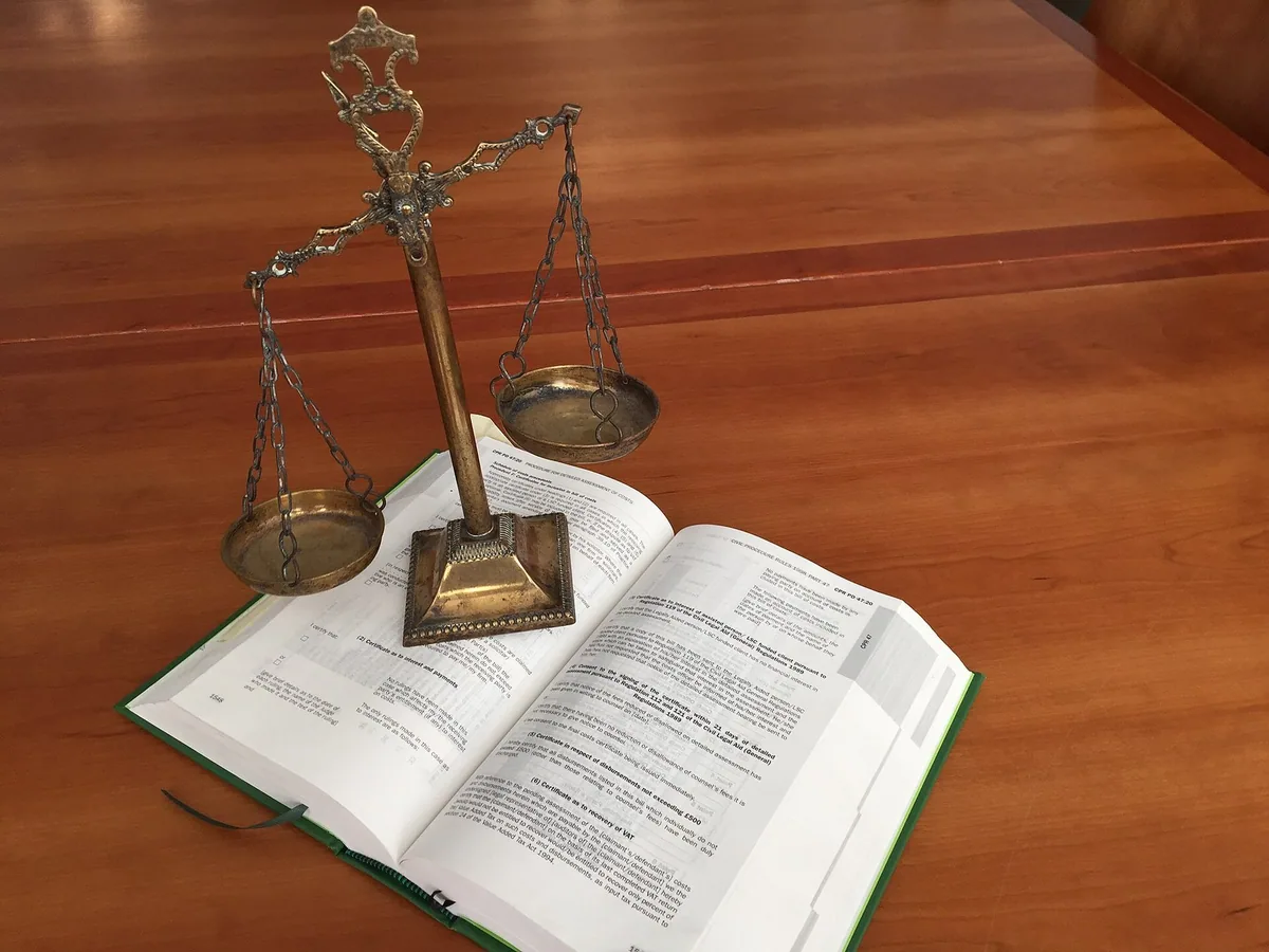 Brass scales of justice standing on an open law book on a polished wooden table
