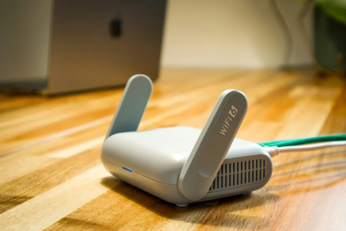 A small white wireless router with two fold-up antennas and network cables plugged in, on a wooden surface