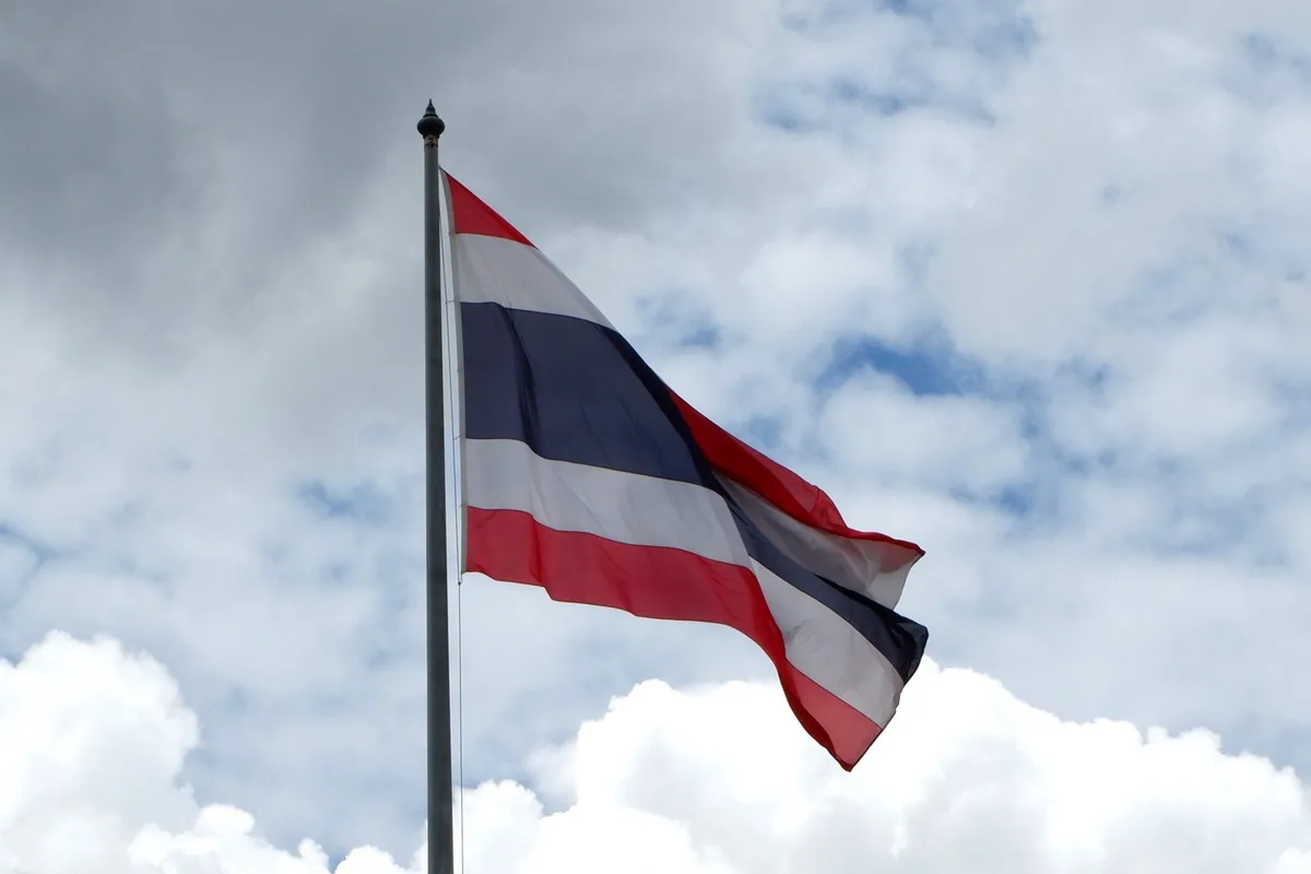 The red, white and blue Thai national flag flying from a tall flagpole against a cloudy sky in Bangkok