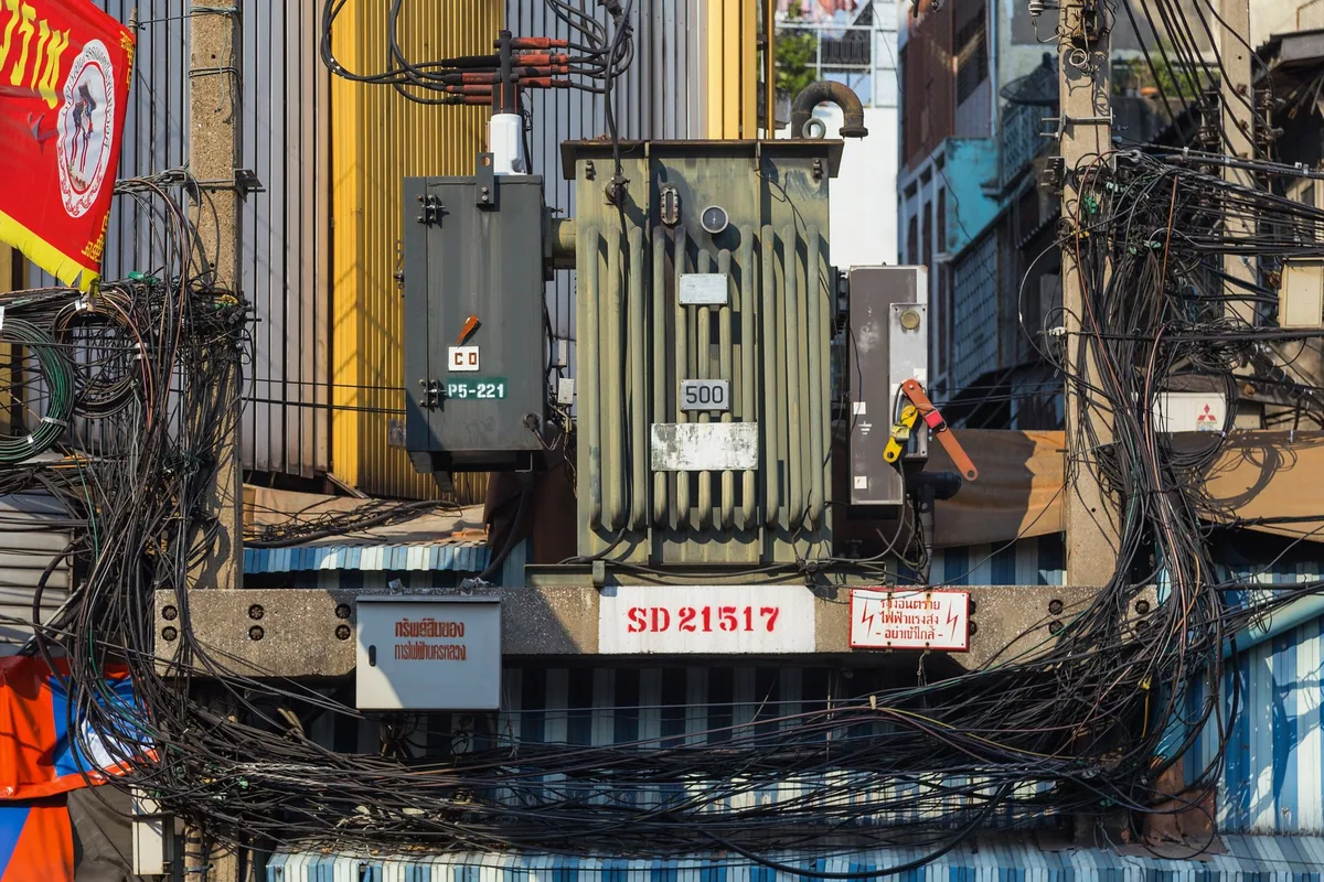 A street transformer on Yaowarat Road in Bangkok wrapped in a tangle of black power and telephone cables