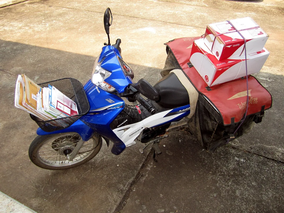 Thailand Post delivery motorbike with a basket of letters and boxed parcels strapped onto red mail panniers