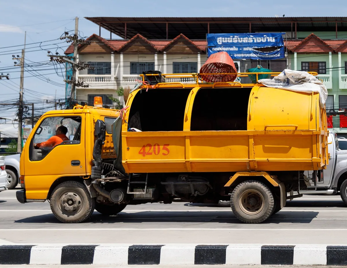 A yellow municipal rubbish collection truck driving along a street in Chiang Rai, northern Thailand