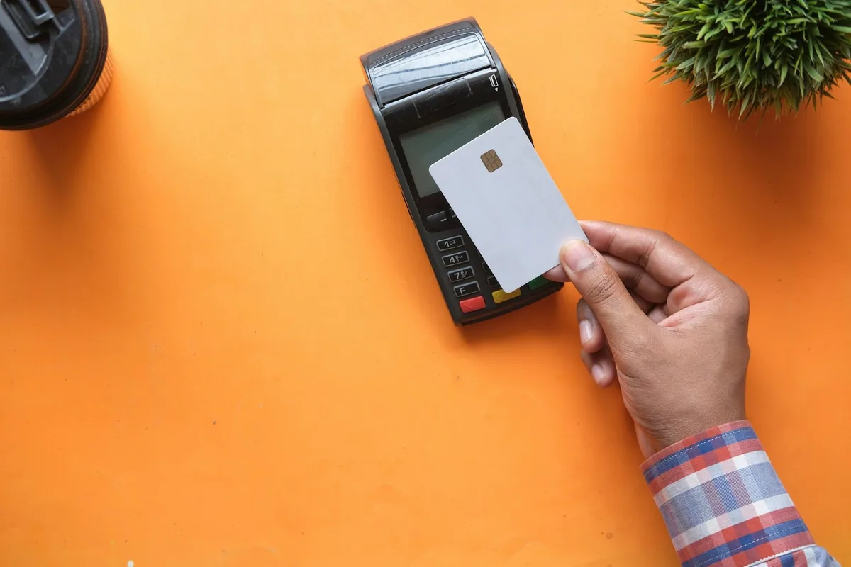 A hand holding a blank chip card next to a card payment terminal on a bright orange table