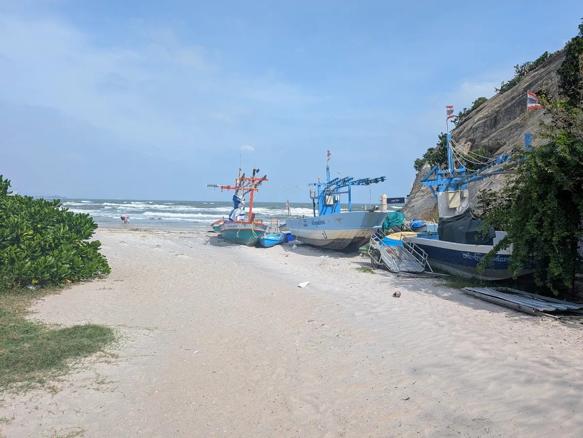 Fishing boats pulled up on a quiet stretch of Hua Hin beach below a rocky headland