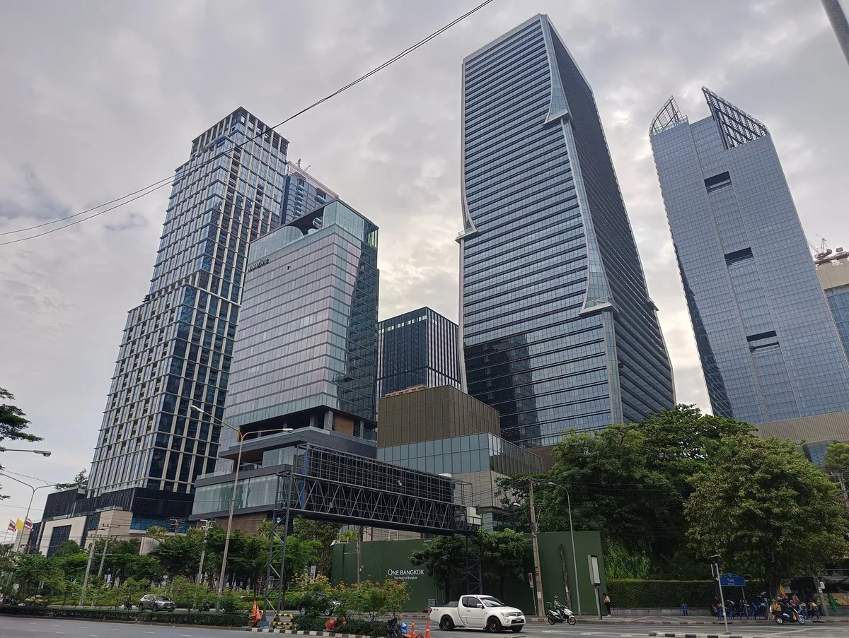 New glass office towers of the One Bangkok complex rising above trees on Rama IV Road in Bangkok