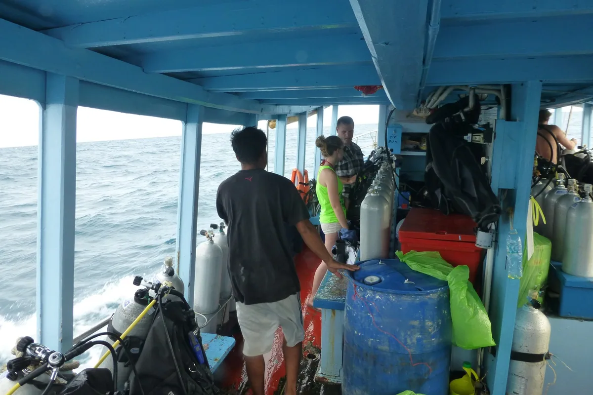 Crew and divers among racks of scuba tanks and gear on the covered deck of a dive boat off Koh Tao