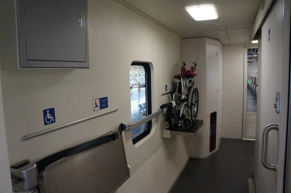 Wheelchair space with a folding seat, grab rail and a stowed wheelchair aboard a State Railway of Thailand carriage