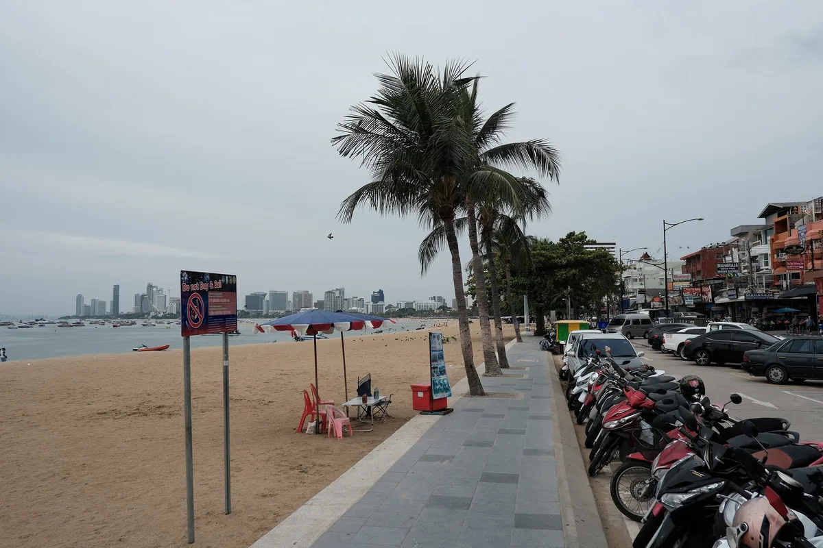 Palm-lined promenade along Pattaya Beach dividing the sand from Beach Road's shops and parked motorbikes