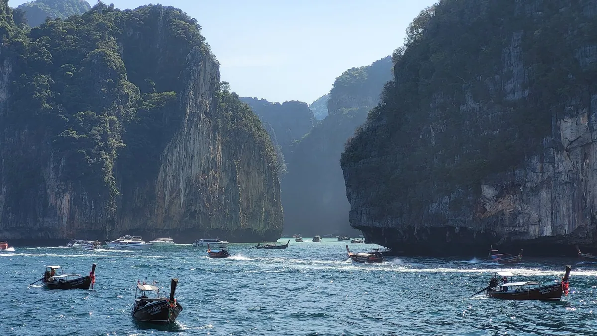 Longtail boats on turquoise water between the sheer limestone cliffs of Ko Phi Phi Le