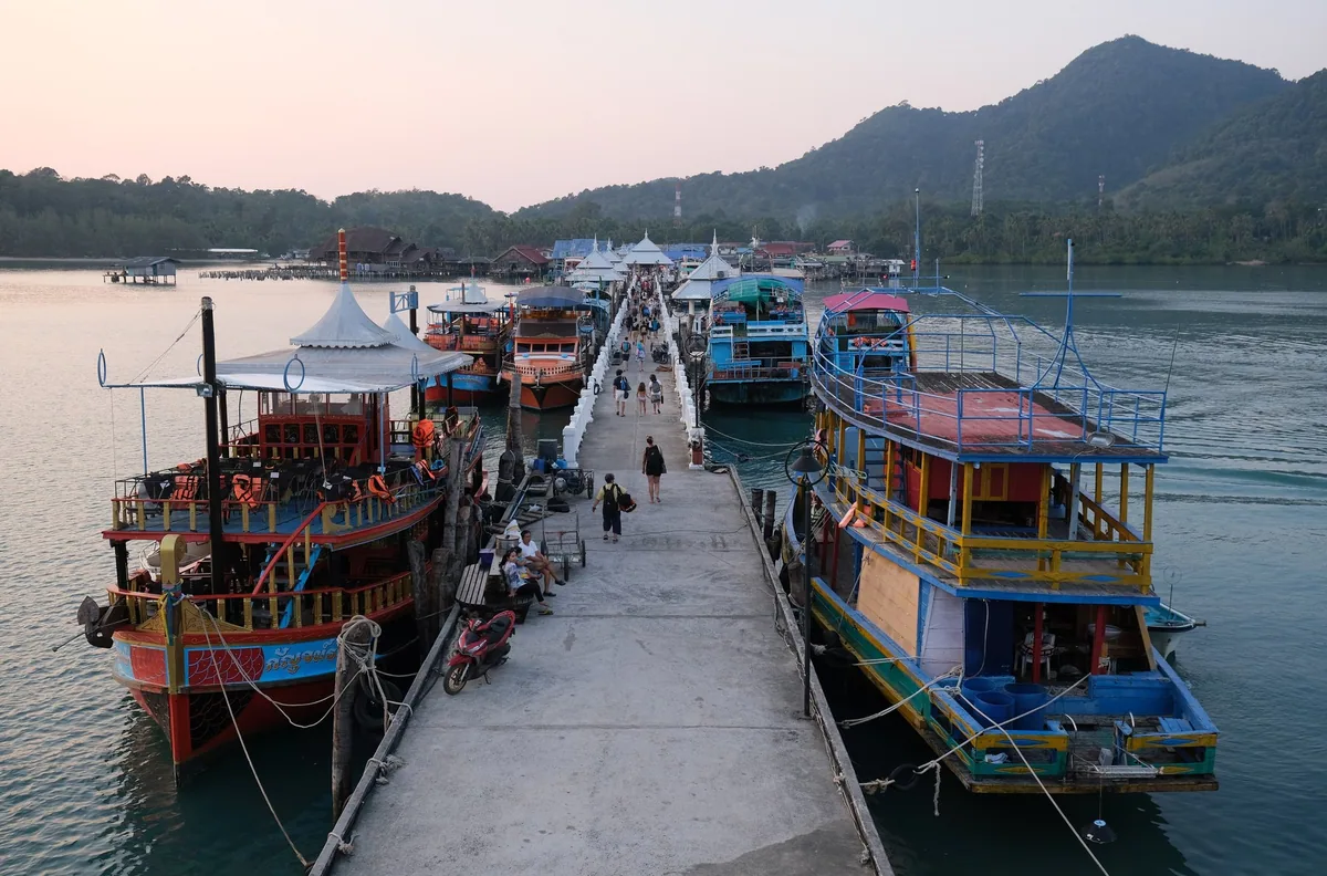Colourful day-trip boats moored along Bang Bao pier on Koh Chang at dusk, with visitors walking out to them