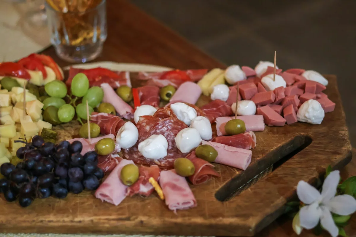 Cured meats, cheese, mozzarella balls, olives and grapes laid out on a wooden board