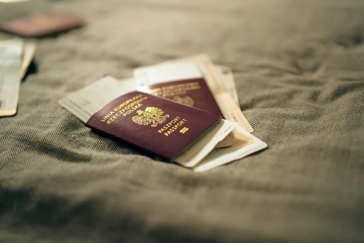 Two burgundy passports with folded travel papers tucked inside lying on a rumpled fabric surface
