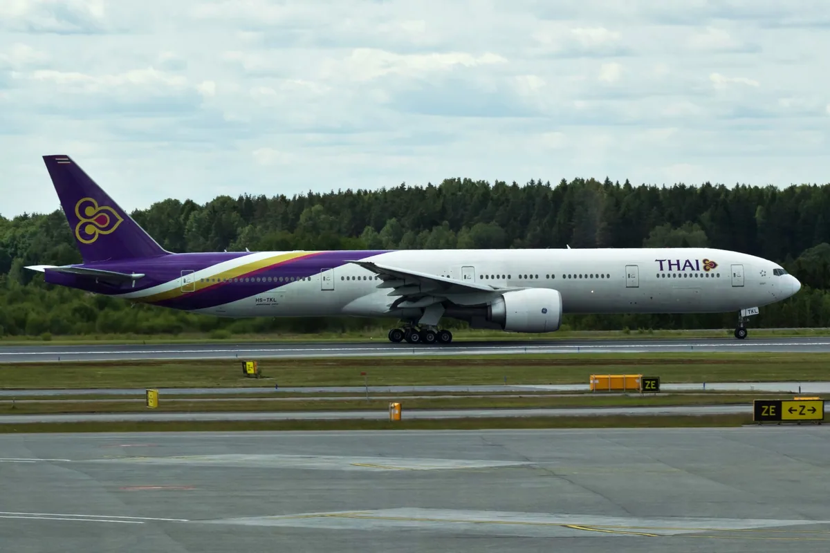 A Thai Airways Boeing 777 on the runway at Stockholm Arlanda Airport, with Swedish pine forest behind