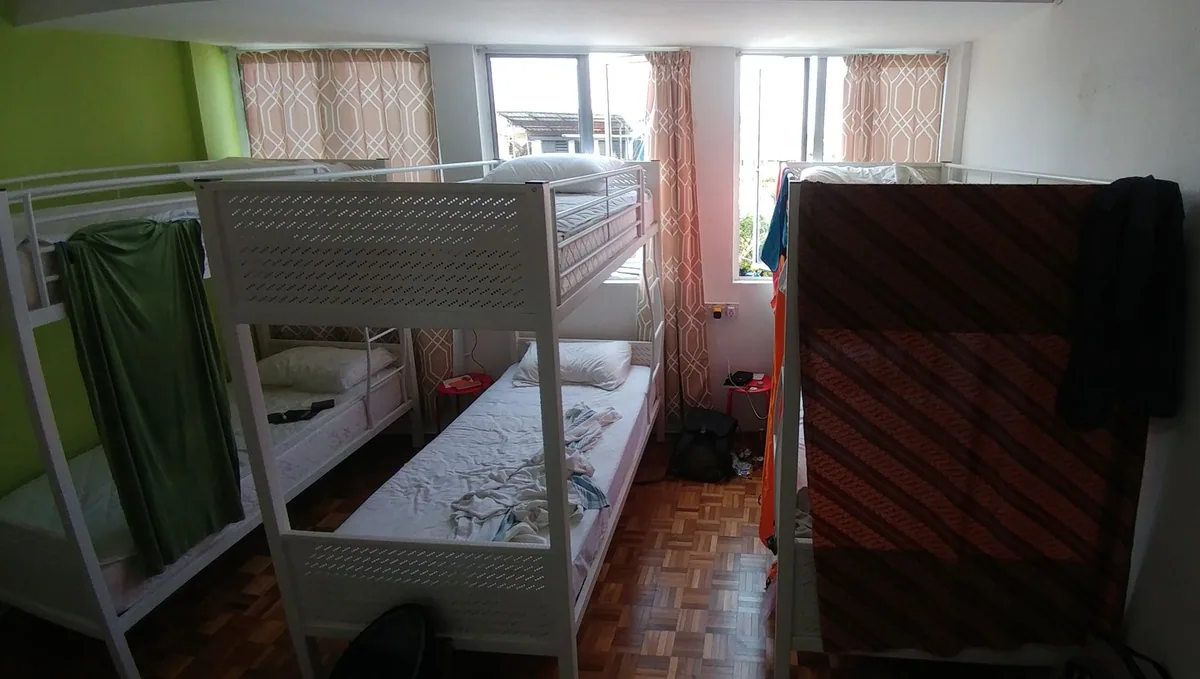 White metal bunk beds in a six-bed hostel dorm, with guests' sarongs hung as privacy curtains