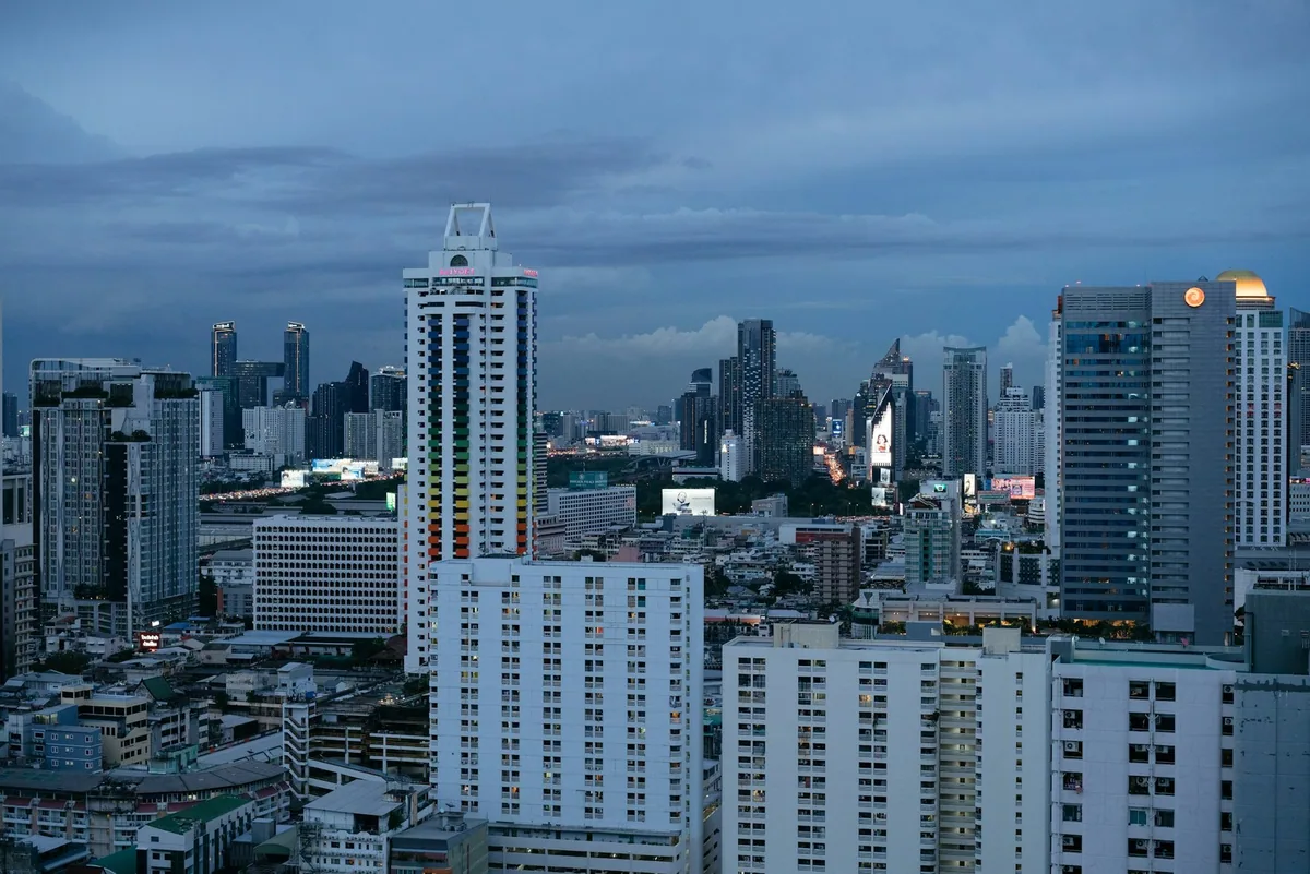 Dense blocks of apartment and condominium towers under a stormy dusk sky in central Bangkok