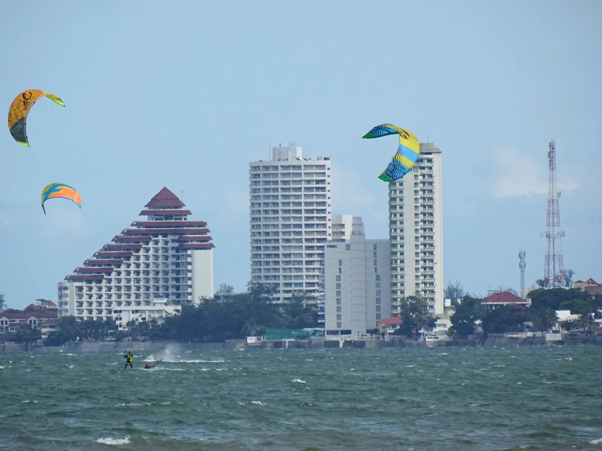 Kitesurfers and colourful kites in a strong wind off Hua Hin, with beachfront hotel towers behind