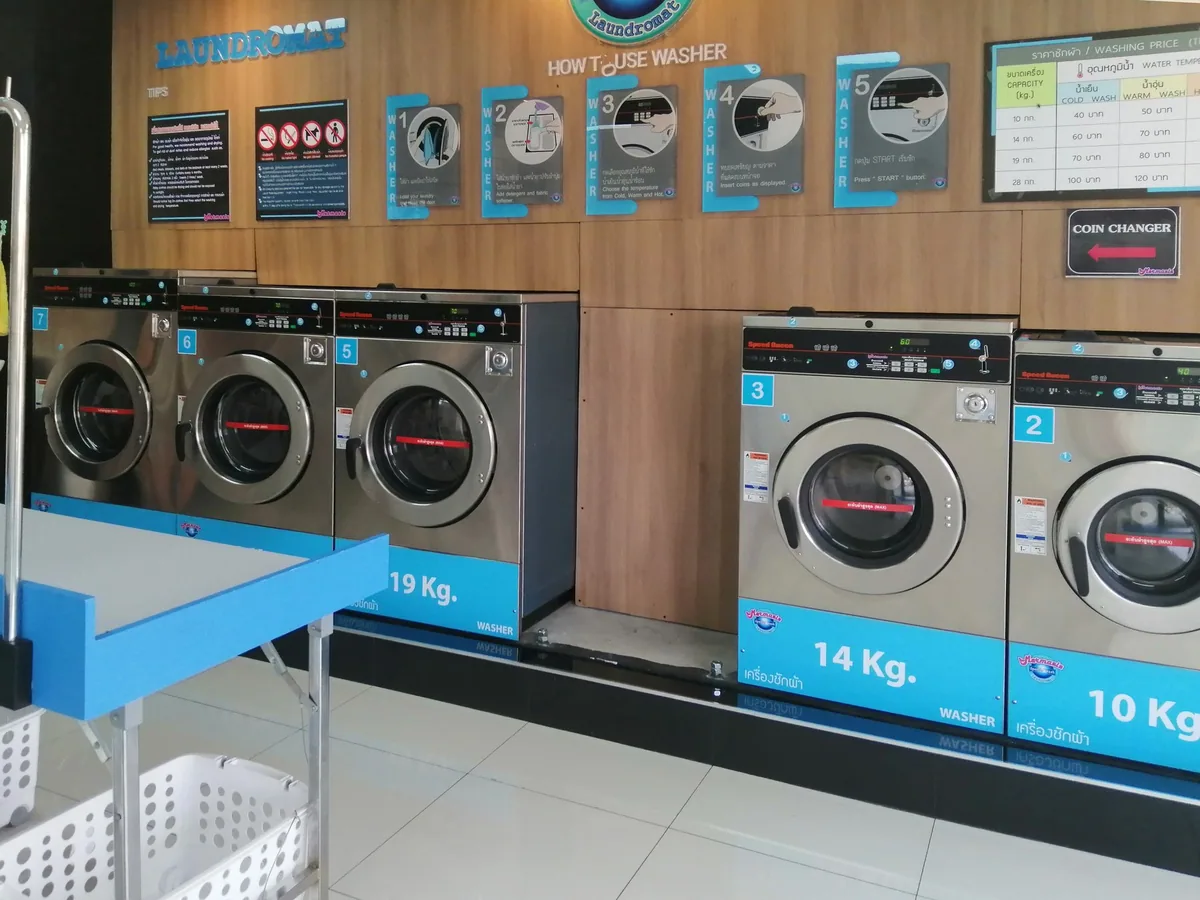Row of coin-operated front-loading washers with Thai and English labels in a self-service laundromat in Chiang Mai