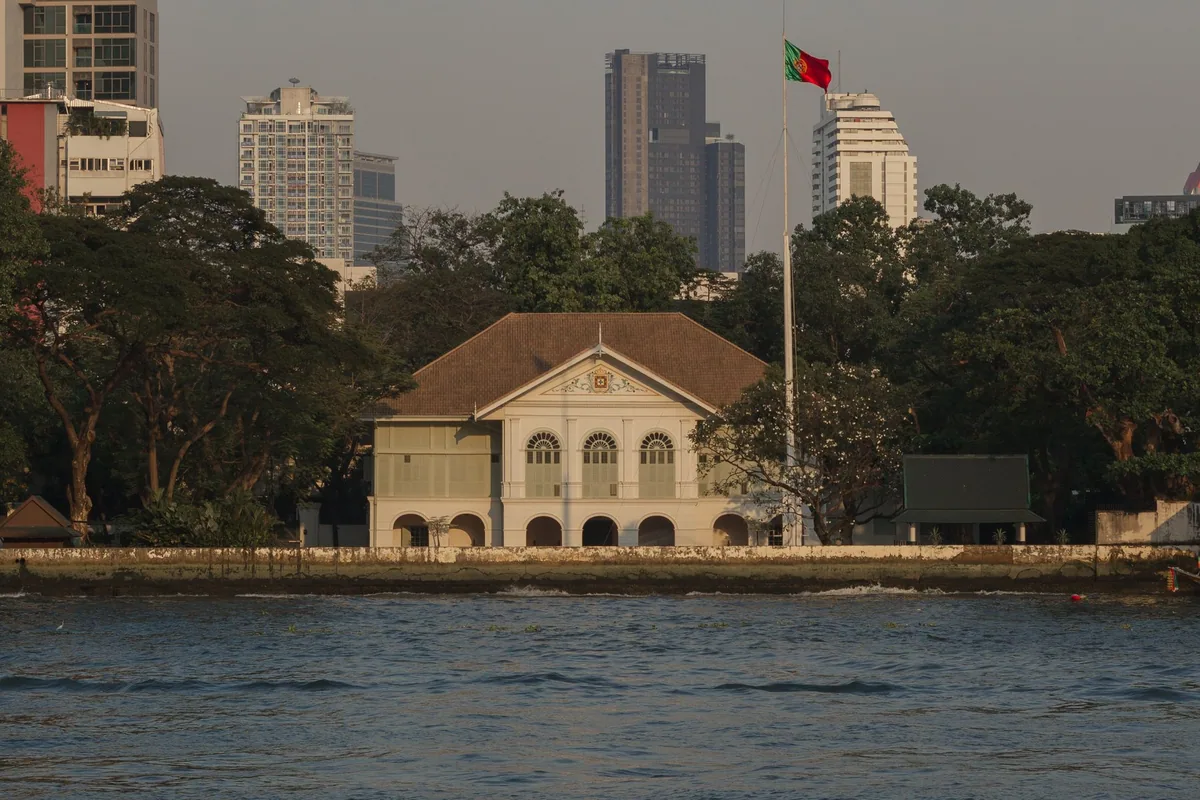 The colonial-era Embassy of Portugal on the Chao Phraya riverbank in Bangkok, with its flag flying above the trees