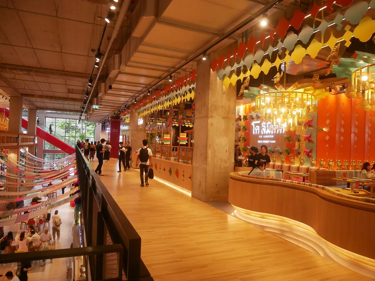 Shoppers walking along a timber-floored upper level of the Emsphere mall in Bangkok, under strings of Thai bunting