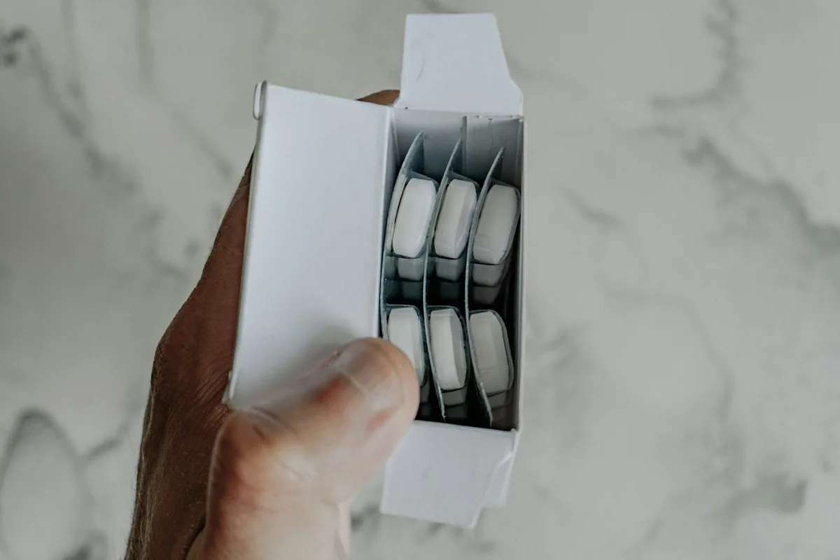A hand opening a box of white tablets in foil blister packaging