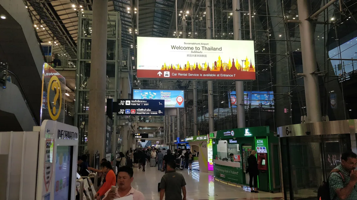 A large Welcome to Thailand sign hanging over travellers in the arrivals hall of Suvarnabhumi Airport