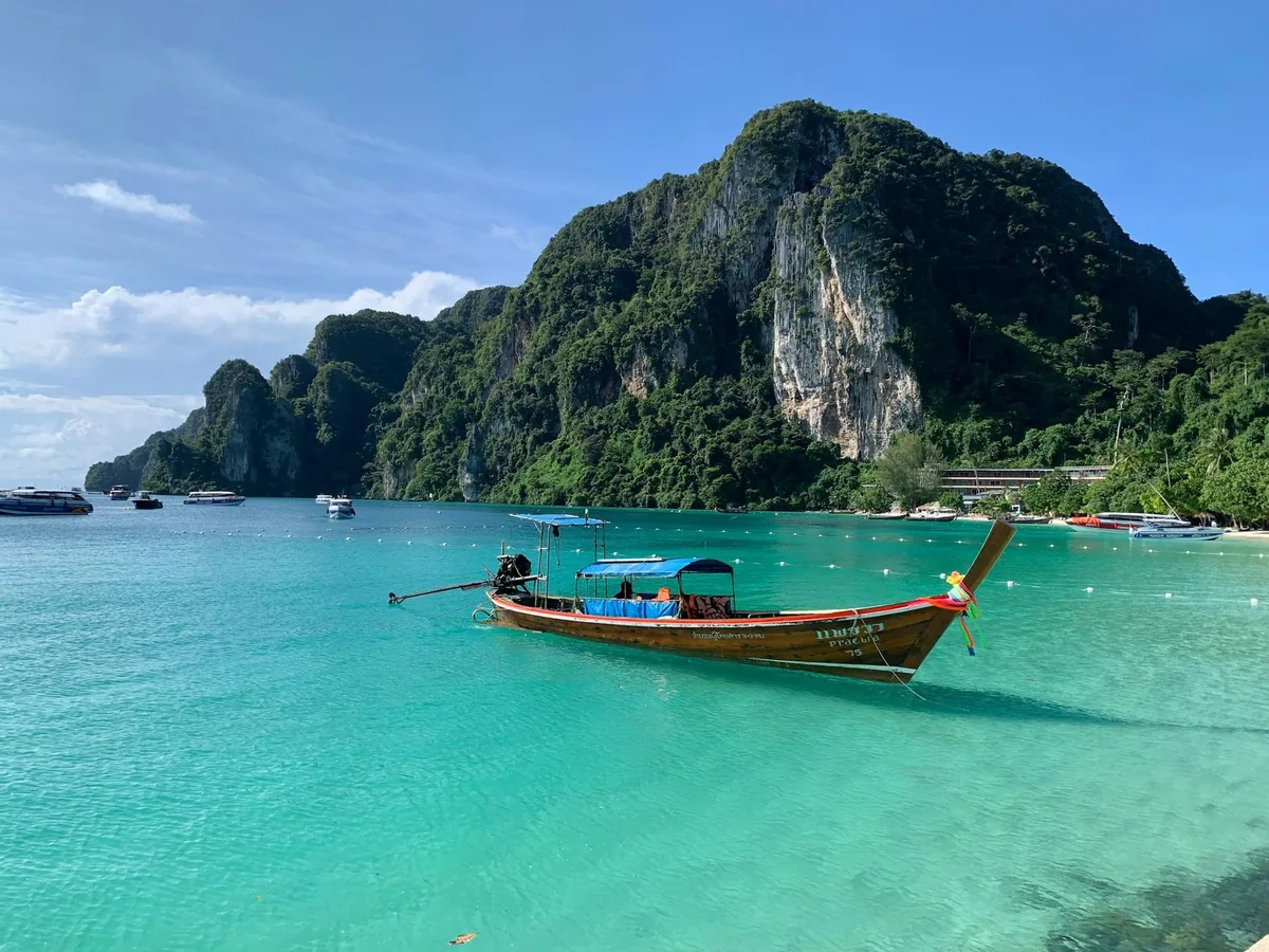 A longtail boat on turquoise water below the limestone cliffs of Koh Phi Phi Don