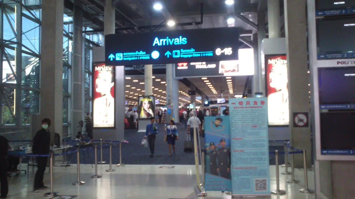 Passengers walking under the overhead Arrivals sign inside Suvarnabhumi Airport, Bangkok