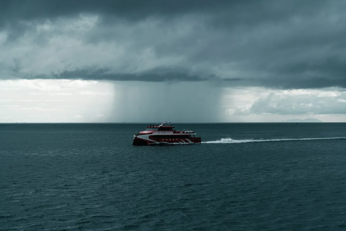 A passenger boat crossing a dark sea beneath a heavy rain squall