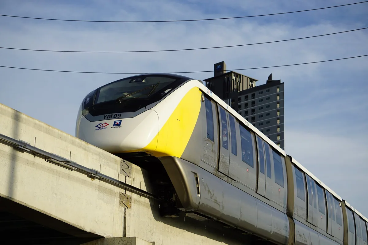 A yellow-and-white MRT Yellow Line monorail train gliding along its elevated concrete beam in Bangkok