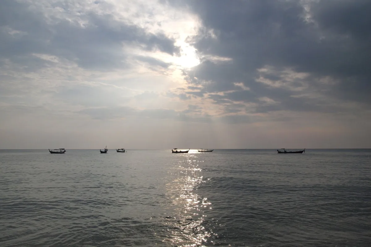 Silhouetted longtail fishing boats on the Andaman Sea off Khao Lak under a cloudy late-afternoon sky