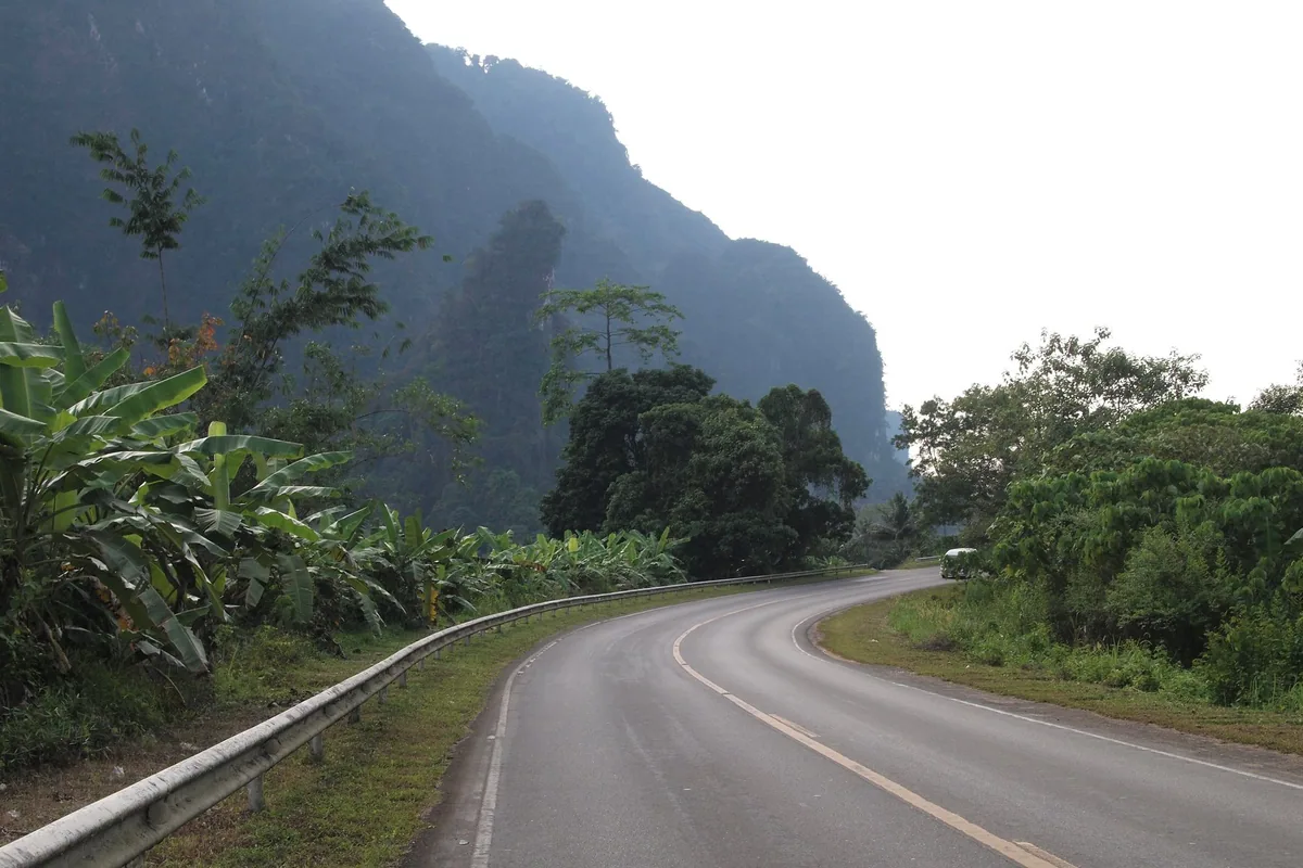Highway 401 curving past banana plants and forested limestone cliffs near Khlong Phanom National Park, Surat Thani